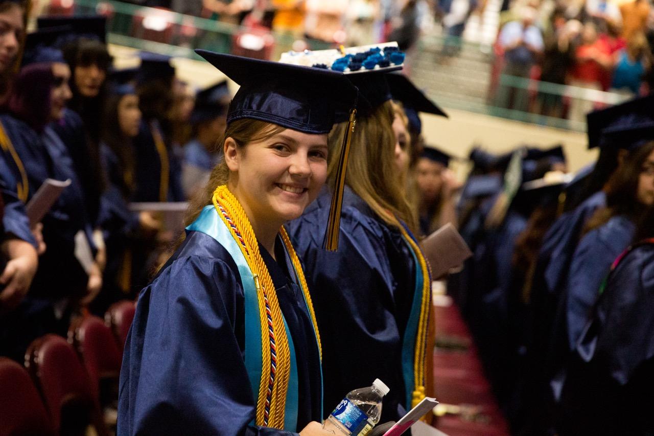 <br />
A female student in a graduation gown  at graduation smiling at the camera.