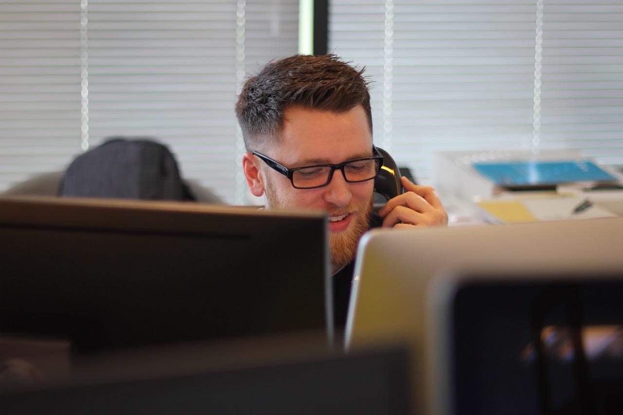 一名戴眼镜的男子坐在电脑前打电话.